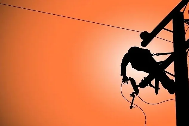 Silhouet van een werknemer die aan een elektriciteitspaal werkt tegen een oranje achtergrond.