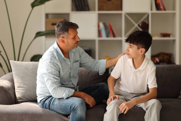Een volwassene praat vriendelijk met een jongere op een bank in een woonkamer.